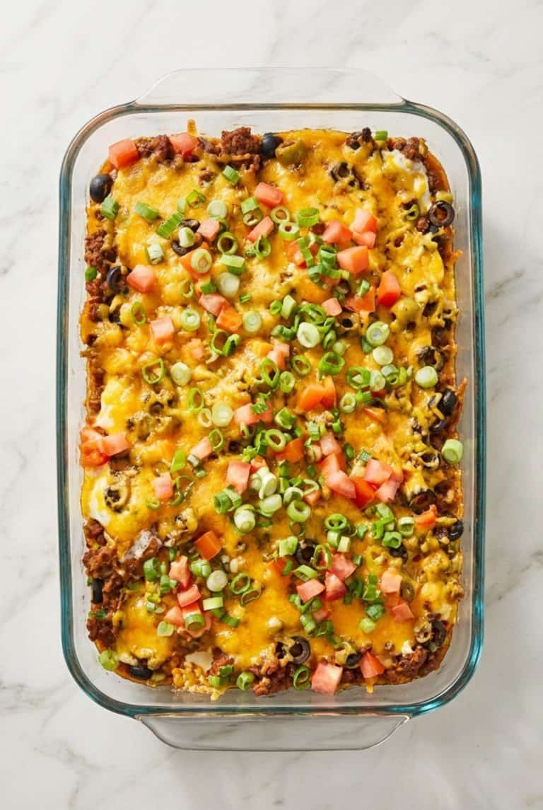 Cheesy taco casserole topped with chopped tomatoes and green onions in a glass baking dish.