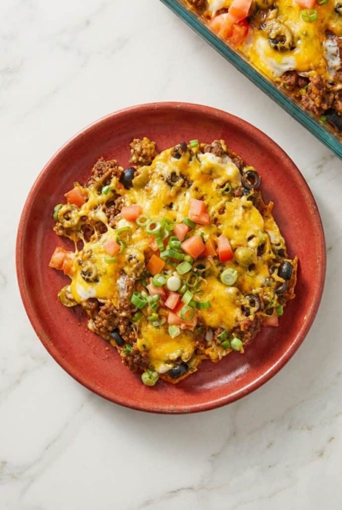 Plated serving of taco casserole with melted cheese, tomatoes, and green onions.