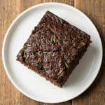 A slice of moist chocolate zucchini cake on a white plate, showing the rich texture and bits of shredded zucchini inside.