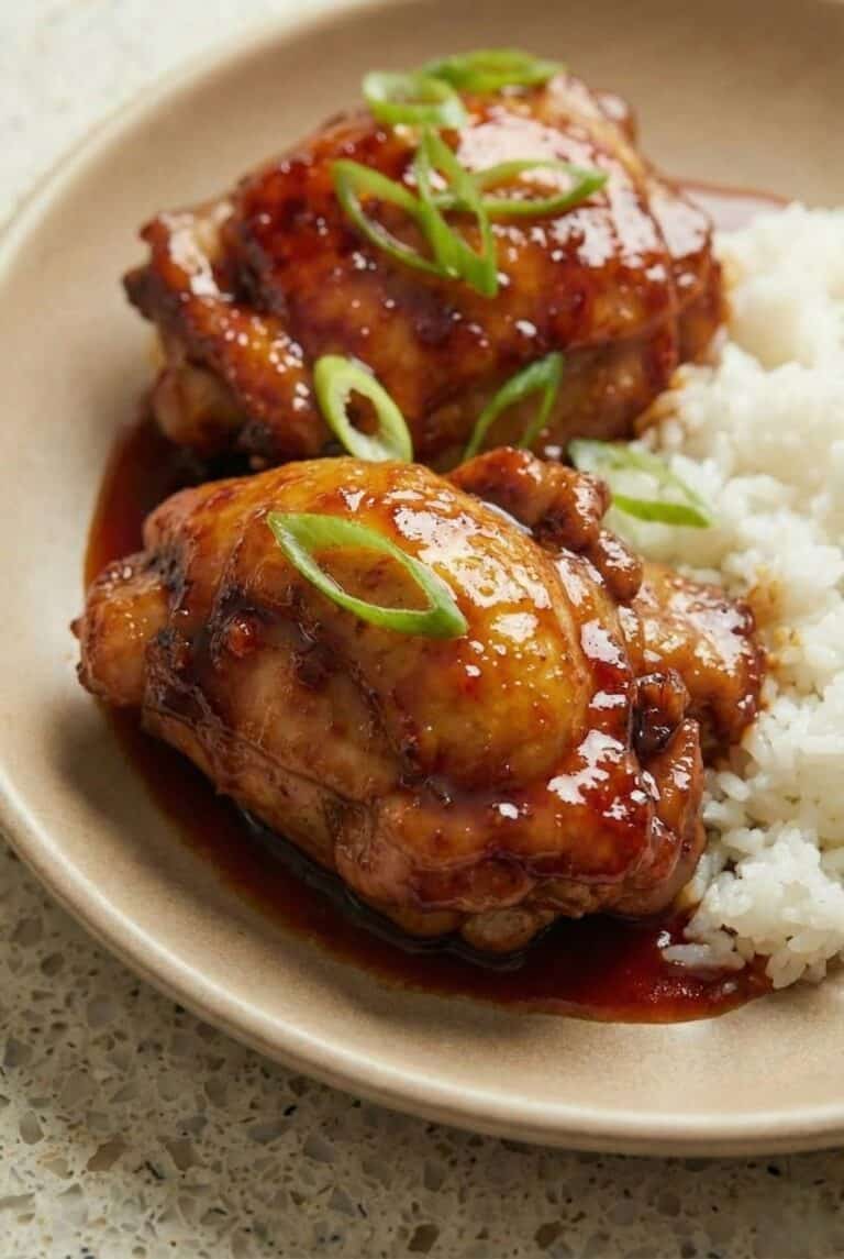 Baked teriyaki chicken thighs glazed in sticky homemade sauce, served over white rice and garnished with sliced green onions.