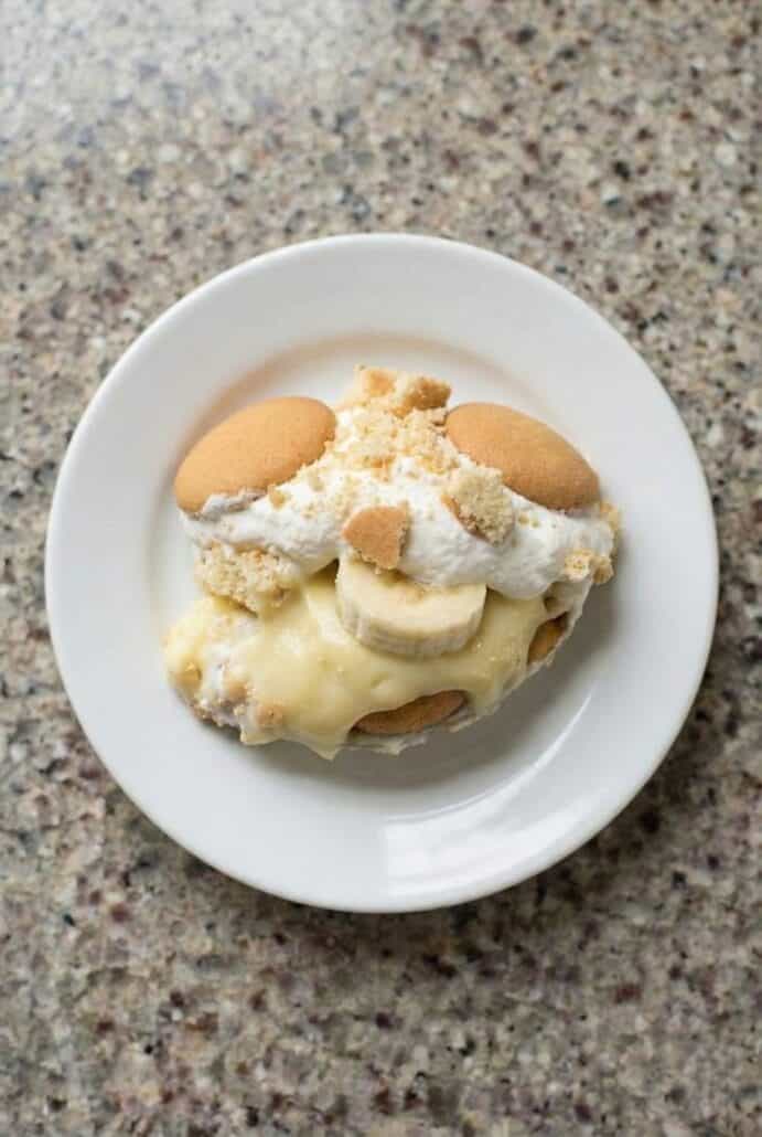 Single serving of banana trifle on a white plate topped with whipped cream and vanilla wafers, showcasing this easy layered no-bake banana dessert recipe.