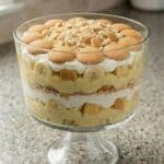 Banana trifle layered with pound cake, banana pudding, whipped cream, and vanilla wafers in a glass trifle bowl.