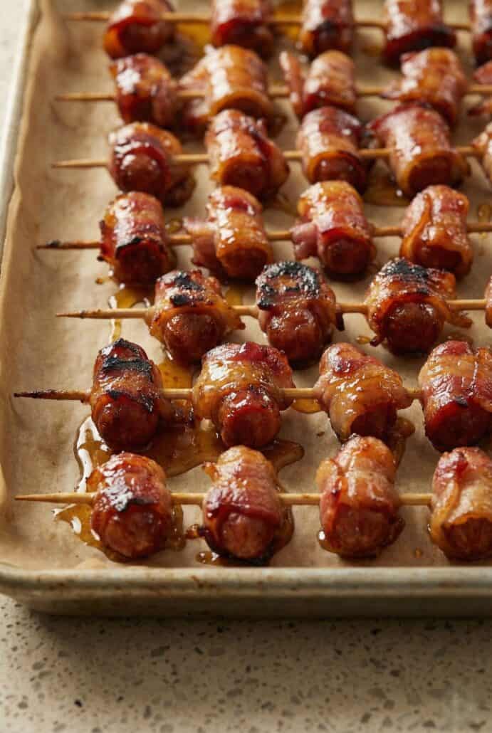 Close-up of bacon-wrapped little smokies caramelized with brown sugar on skewers.