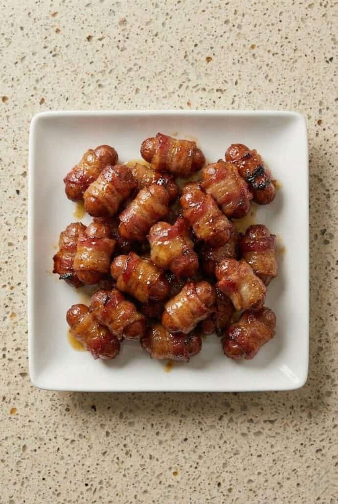 Square white bowl filled with bacon-wrapped little smokies coated in a glossy brown sugar glaze.