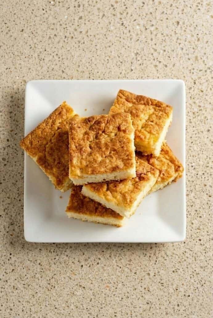 Stack of golden butter swim biscuit squares on a white plate, showing the crispy buttery edges and soft fluffy interior.