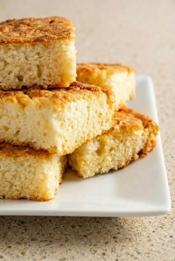 Close-up of stacked butter swim biscuit squares on a plate, highlighting the moist fluffy crumb and crispy golden buttery edges.