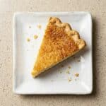 Slice of homemade buttermilk pie with a golden custard filling on a white plate.