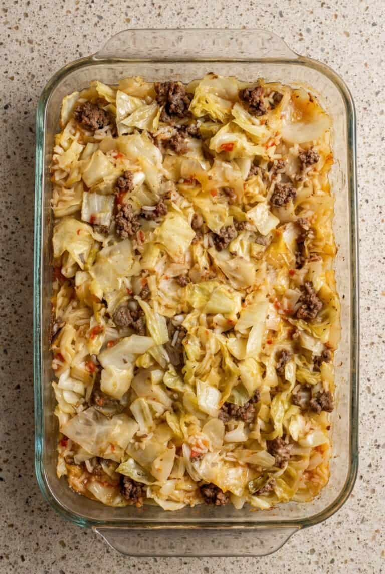 Overhead image of hearty cabbage roll casserole baked in a glass dish, showing tender cabbage, ground beef, and rice in rich tomato sauce.