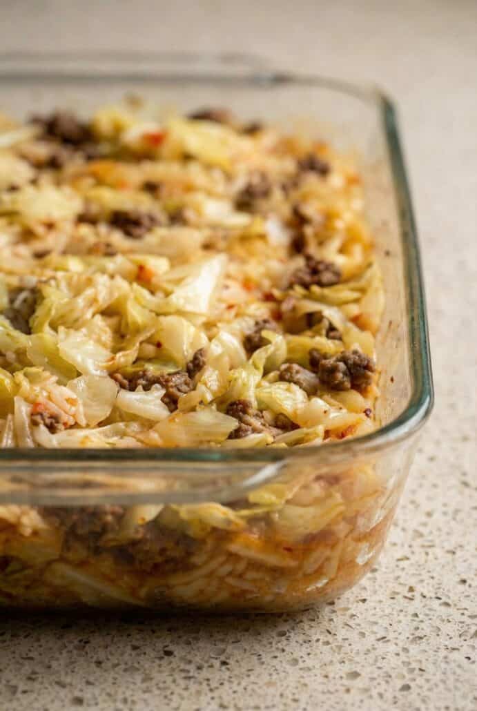 Side view of baked cabbage roll casserole in a glass baking dish, layered with ground beef, rice, and tender cabbage in tomato sauce.
