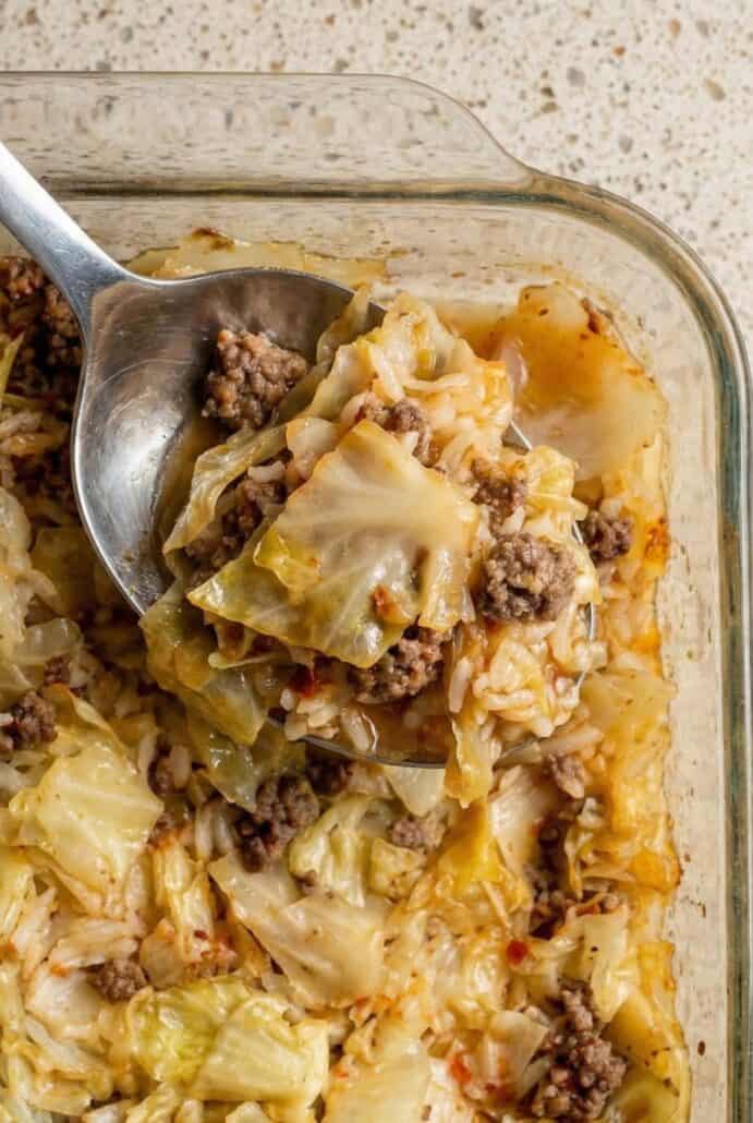 Close-up image of a spoon scooping cabbage roll casserole from a glass baking dish.