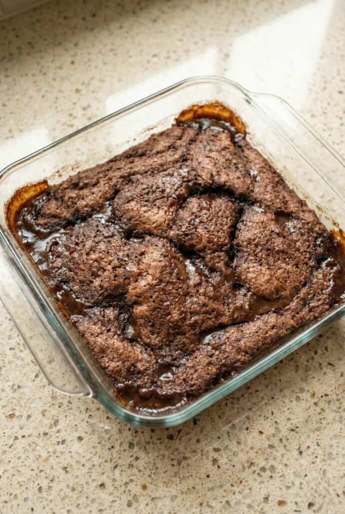 Close-up overhead image of homemade chocolate cobbler in a glass baking dish, highlighting the crackled chocolate cake top and rich self-saucing layer baked underneath.