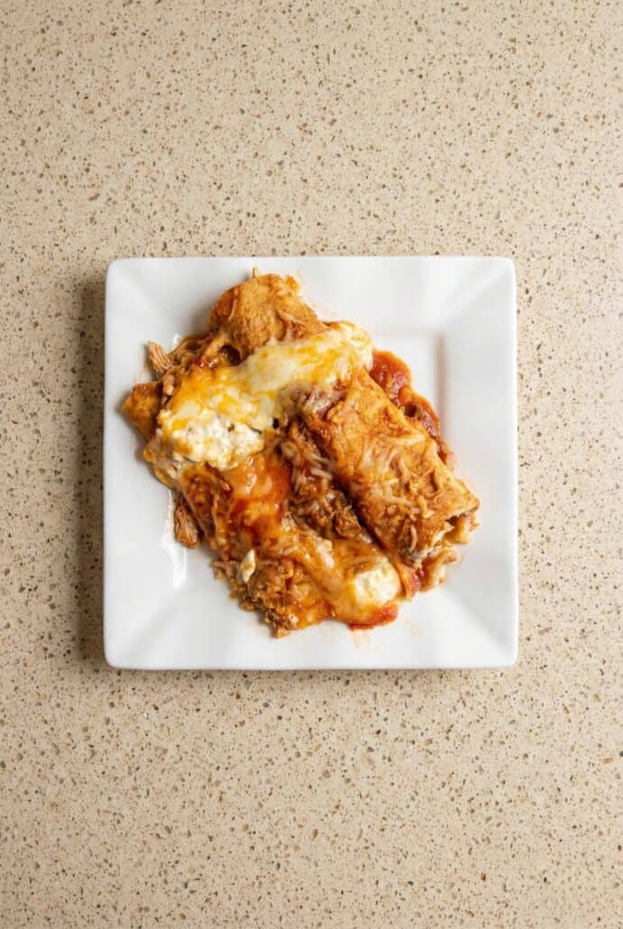 Plated Cottage Cheese Chicken Enchiladas topped with melted cheese and red sauce.