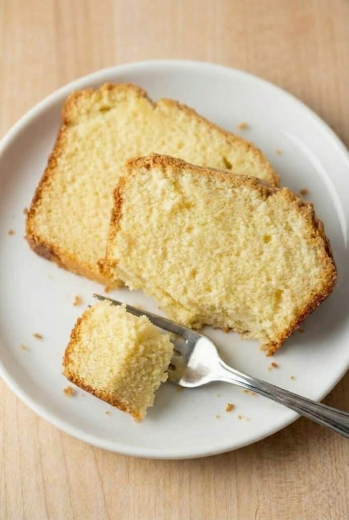 Slices of cream cheese pound cake on a plate with a fork, showing a piece being lifted with the fork to highlight the cake’s moist, fluffy texture.