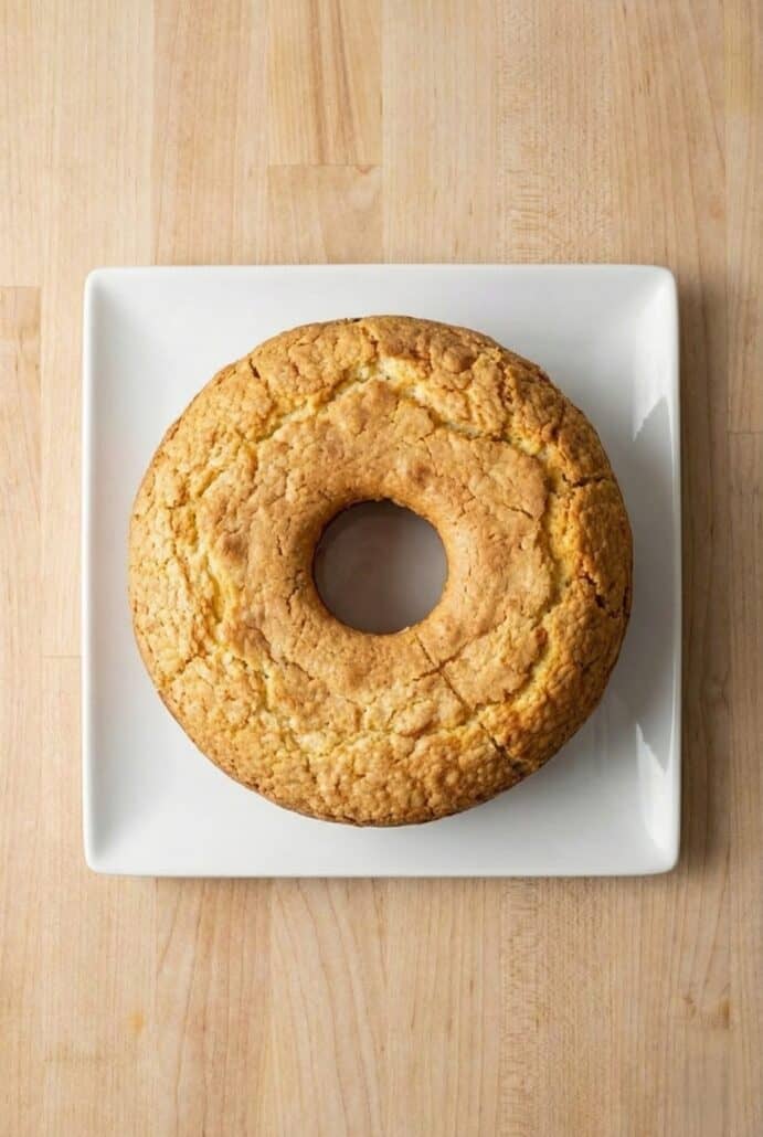 Top view of a whole cream cheese pound cake on a square plate, showcasing its golden-brown crust and soft, airy texture.