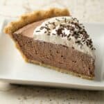 Slice of creamy chocolate mousse pie with whipped topping and chocolate curls on a white plate, highlighting the rich and fluffy texture.
