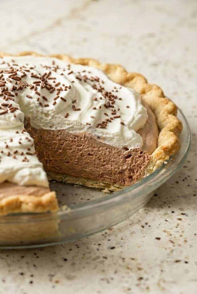 Close-up slice of creamy chocolate mousse pie with fluffy whipped topping and chocolate shavings in a flaky crust.