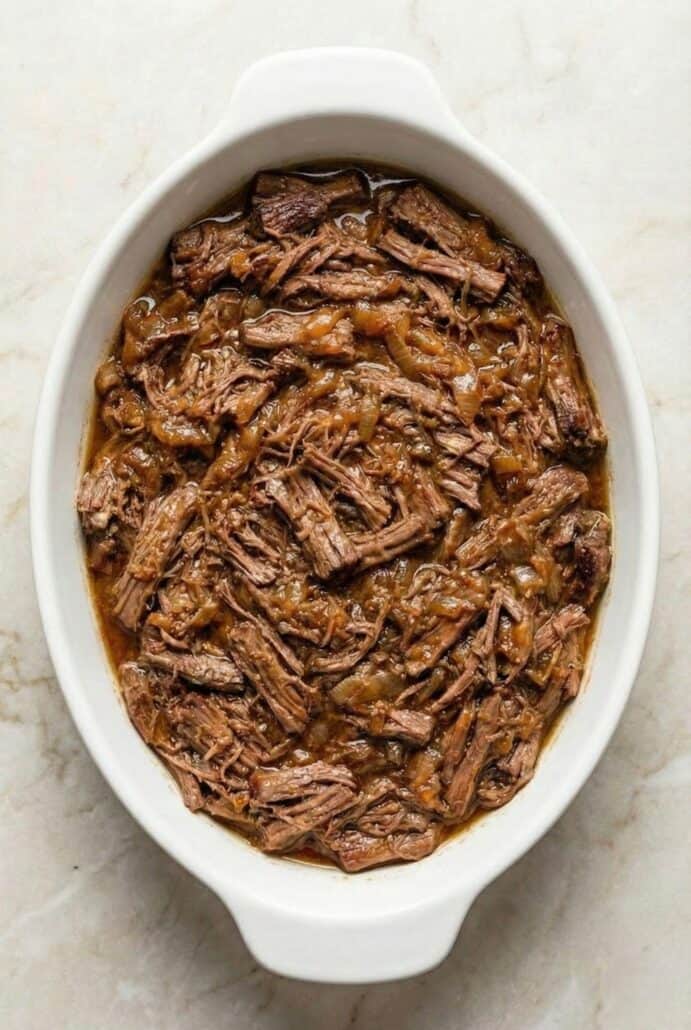 Slow cooker Georgia pot roast with shredded beef and rich gravy in a white casserole dish, highlighting the tender, fall-apart texture of this easy crockpot dinner recipe.
