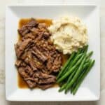 Georgia pot roast with mashed potatoes and green beans, showing tender shredded beef in rich gravy.