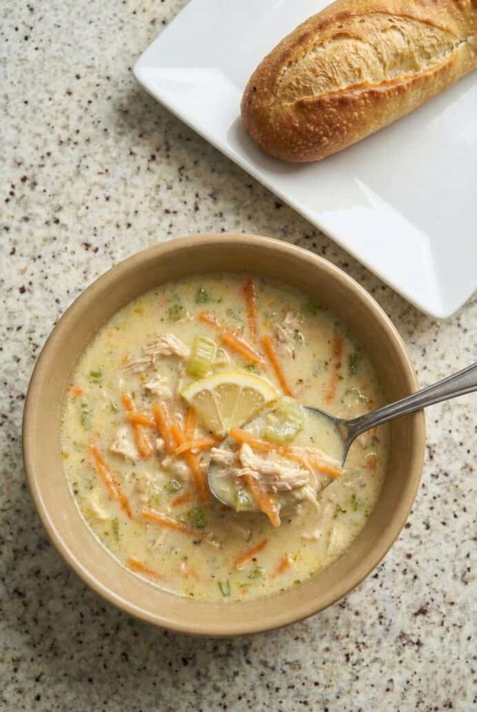 Close-up of creamy Greek lemon chicken soup with rice and shredded carrots, shown being scooped with a spoon to highlight the rich, silky avgolemono texture.