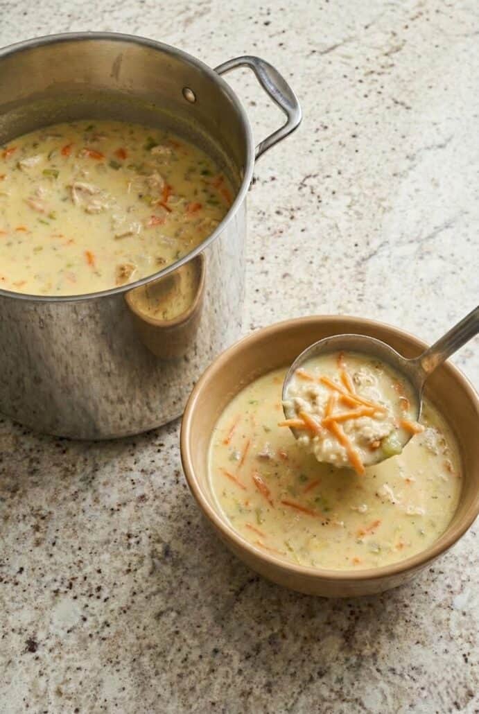 Bowl of homemade Greek lemon chicken soup with rice and shredded carrots served from a large pot.