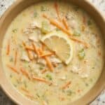 Bowl of creamy Greek lemon chicken soup (avgolemono) topped with fresh lemon slice, shredded carrots, and herbs.