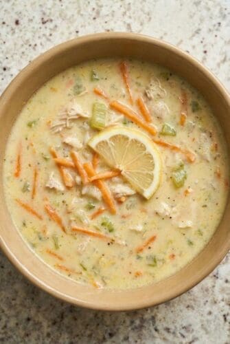 Bowl of creamy Greek lemon chicken soup (avgolemono) topped with fresh lemon slice, shredded carrots, and herbs.