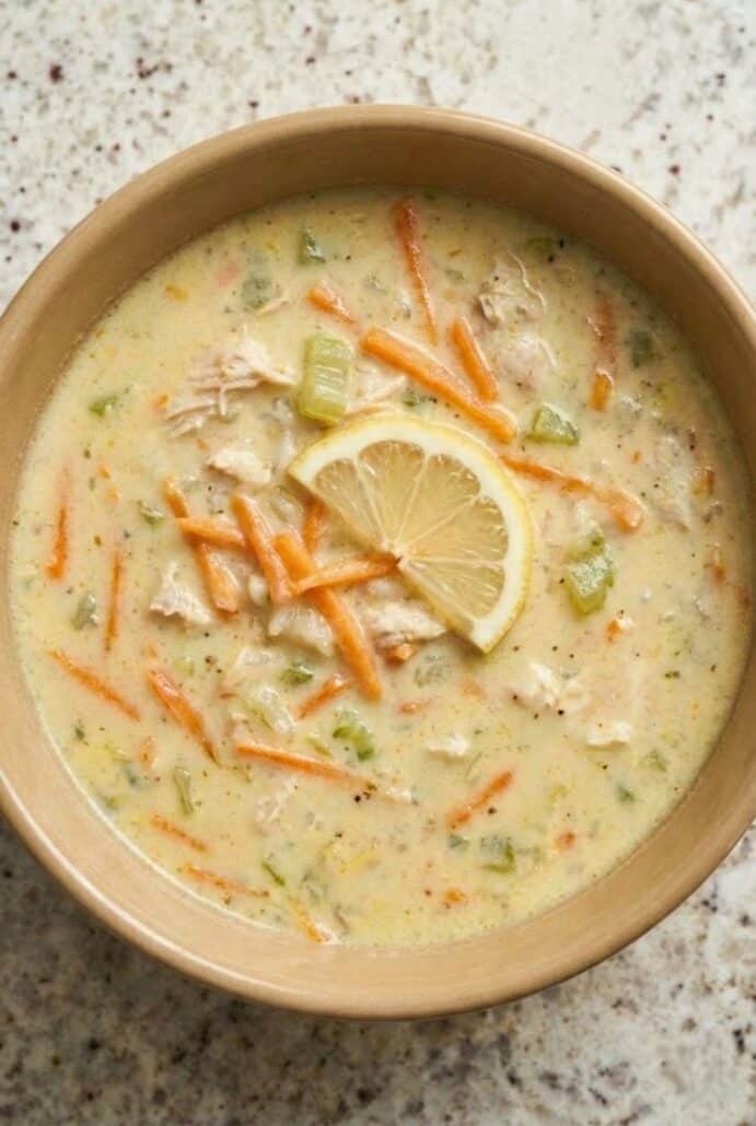 Bowl of creamy Greek lemon chicken soup (avgolemono) topped with fresh lemon slice, shredded carrots, and herbs.