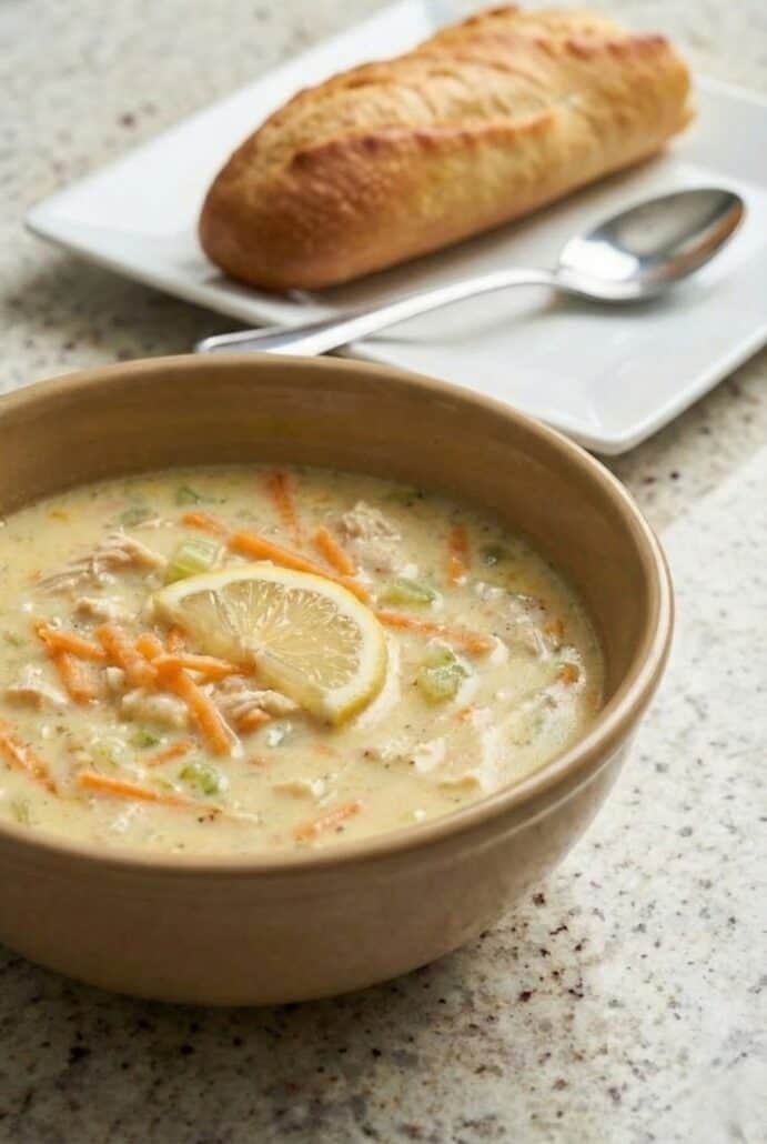 Creamy Greek lemon chicken soup garnished with a fresh lemon slice and shredded carrots, featured as the finished avgolemono recipe.