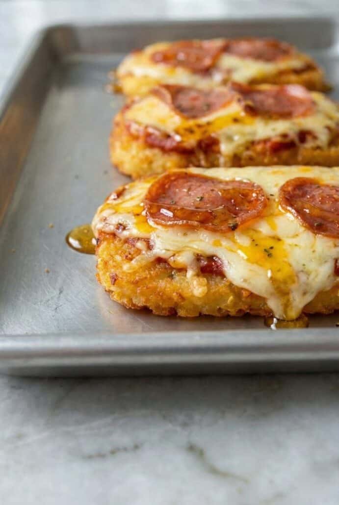 Close-up of crispy hashbrown pizza stacks layered with melted mozzarella and pepperoni on a baking sheet.