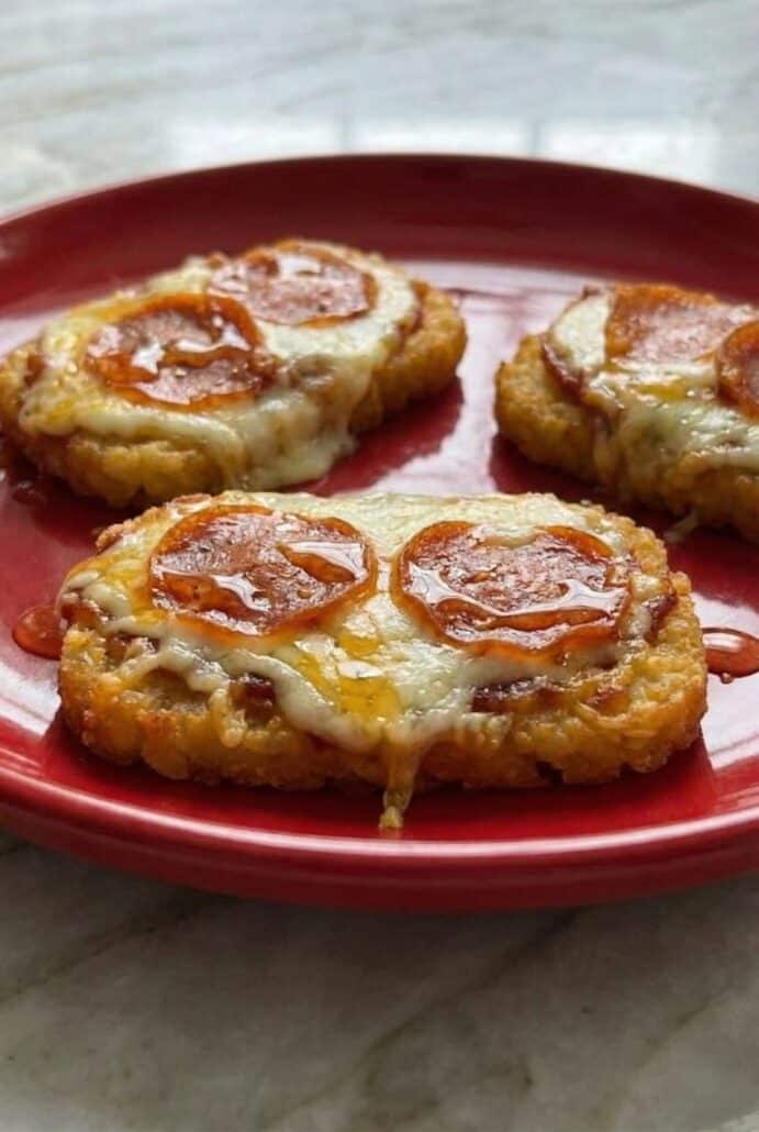 Crispy hashbrown pizza rounds topped with melted mozzarella and pepperoni, served on a red plate.