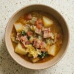 Top view of homemade Irish bacon and cabbage soup in a bowl, filled with tender potatoes, diced bacon, tomatoes, and fresh cabbage.