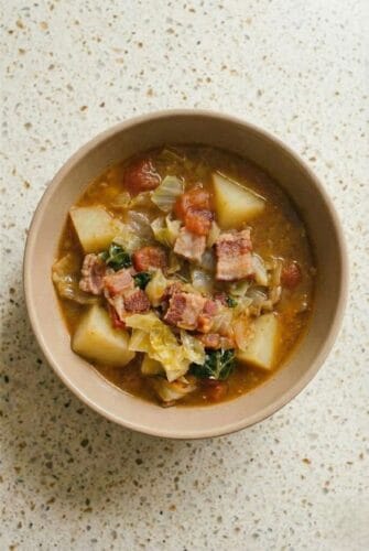 One Pot Irish Bacon Cabbage Soup Recipe Top view of homemade Irish bacon and cabbage soup in a bowl, filled with tender potatoes, diced bacon, tomatoes, and fresh cabbage.