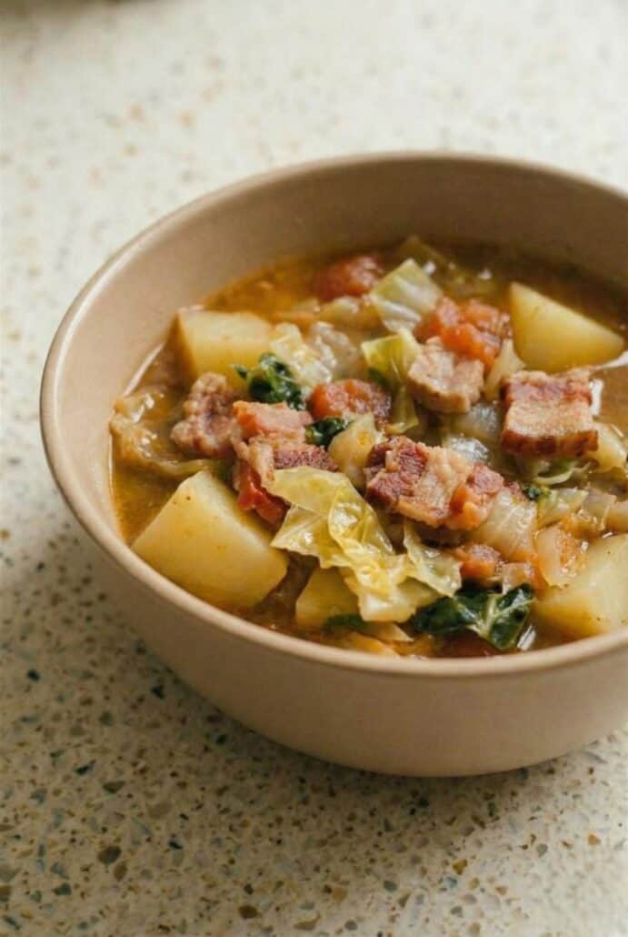 Bowl of Irish bacon and cabbage soup with potatoes, tomatoes, and Savoy cabbage, showcasing the hearty texture and rustic ingredients.