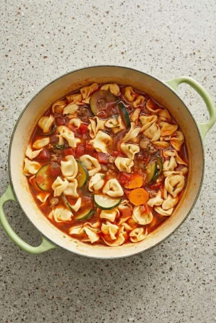Overhead view of Italian sausage tortellini soup simmering in a Dutch oven with carrots and zucchini.