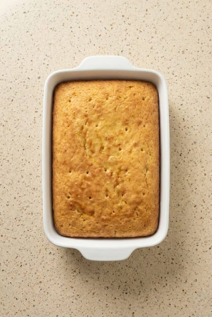 Slice of lemon poke cake topped with white frosting and a fresh lemon slice.