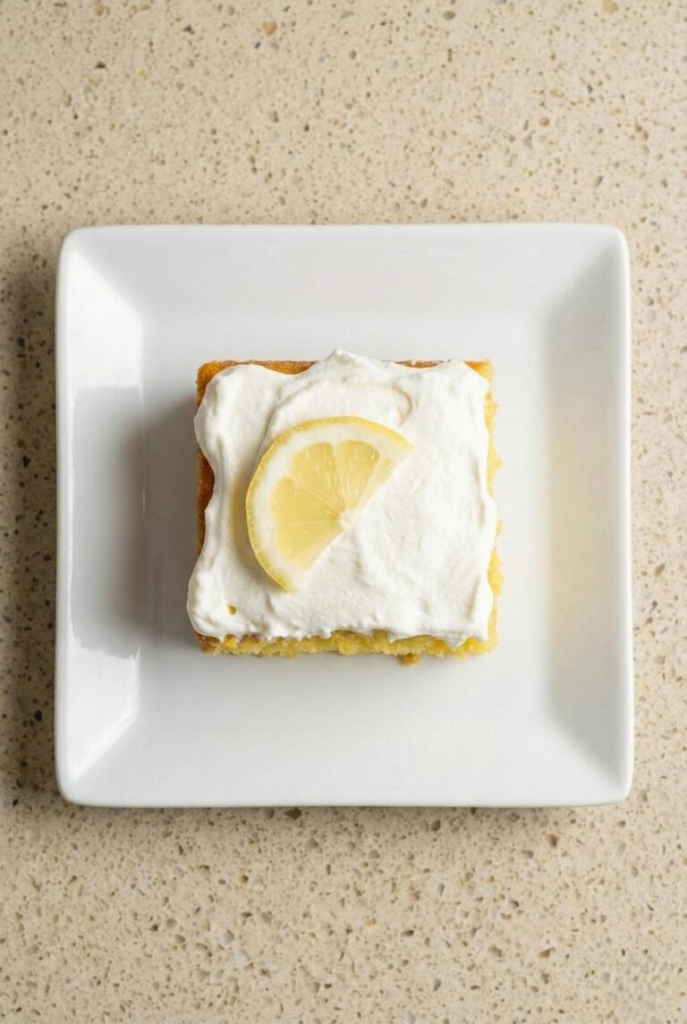 Slice of lemon poke cake topped with white frosting and a fresh lemon slice.