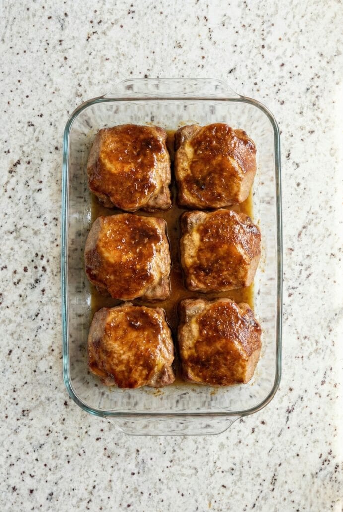 Glass baking dish filled with marinated baked pork chops coated in sweet and savory sauce.