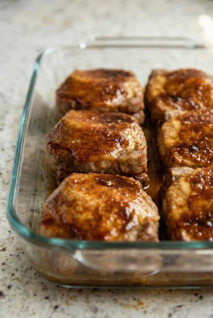 Close-up of juicy marinated baked pork chops in a glass baking dish, coated in a caramelized sweet and savory glaze.
