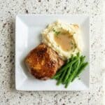 Overhead view of glazed baked pork chop plated with mashed potatoes and green beans.