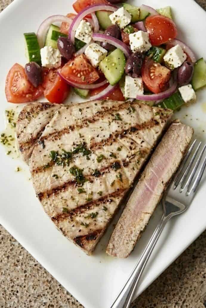 Grilled marinated tuna steak sliced to show a slightly pink center, served with a fresh tomato, cucumber, and red onion salad for this easy healthy dinner recipe.