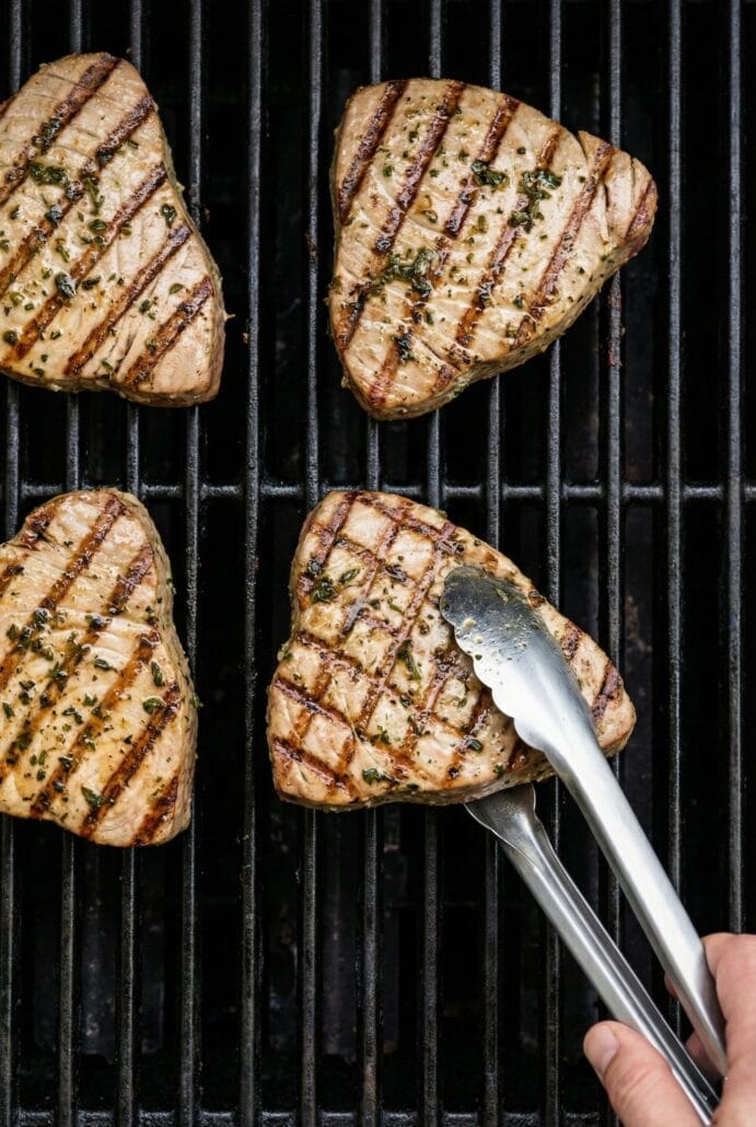 Tuna steaks grilling on an outdoor grill with visible sear marks, demonstrating how to cook marinated tuna.