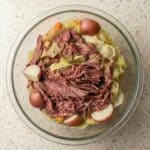 Bowl of slow cooker corned beef and cabbage with shredded brisket, red potatoes, and carrots served in flavorful broth.