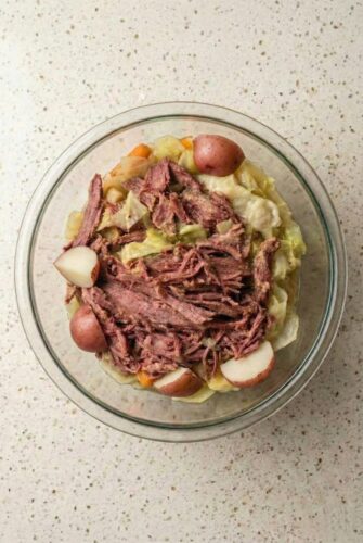 Easy Slow Cooker Corned Beef And Cabbage Recipe Bowl of slow cooker corned beef and cabbage with shredded brisket, red potatoes, and carrots served in flavorful broth.