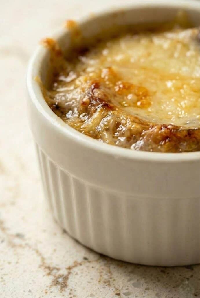 Slow Cooker French Onion Soup in a ceramic ramekin topped with golden, bubbly melted cheese.