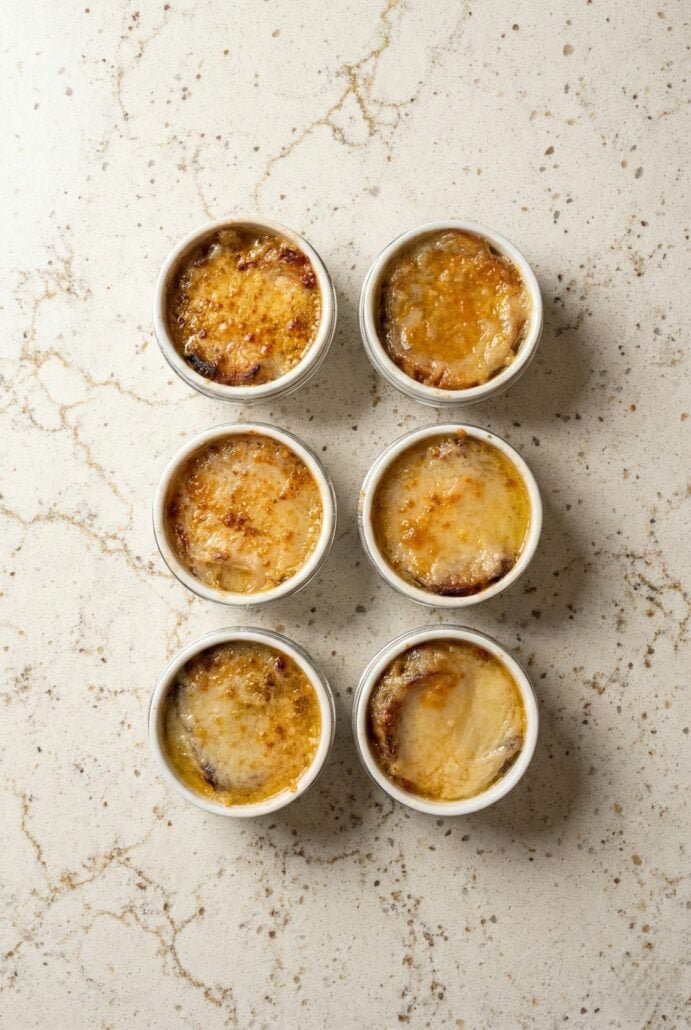 Overhead view of individual ramekins filled with Slow Cooker French Onion Soup, topped with toasted bread and golden melted cheese.