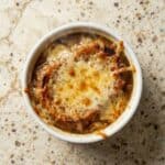 Close-up of Slow Cooker French Onion Soup in a ramekin with deeply caramelized onions and a golden, bubbly cheese topping.