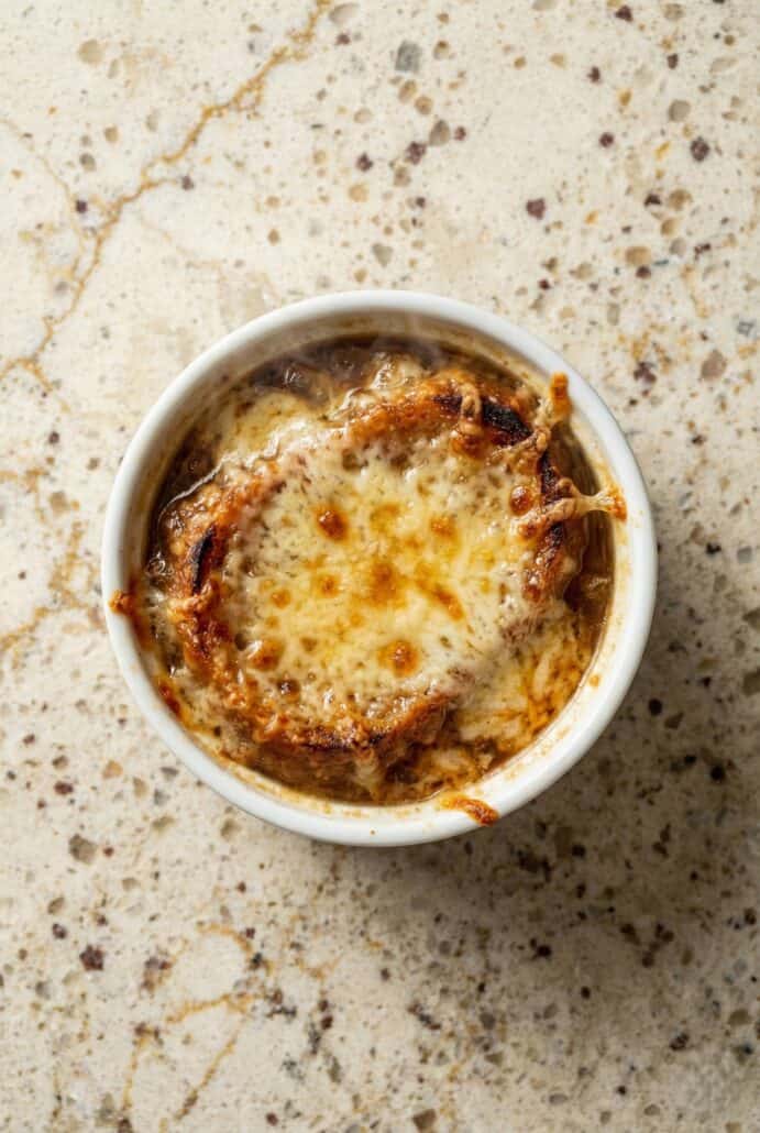 Close-up of Slow Cooker French Onion Soup in a ramekin with deeply caramelized onions and a golden, bubbly cheese topping.