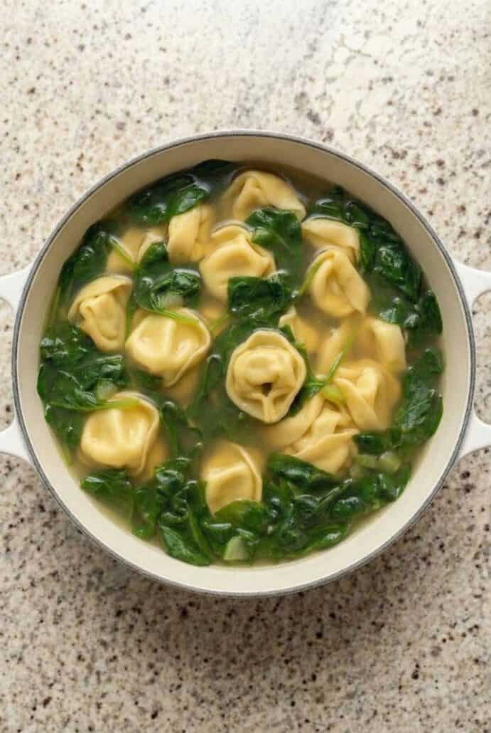Overhead photo of homemade spinach tortellini soup with cheese tortellini and leafy spinach in savory broth.