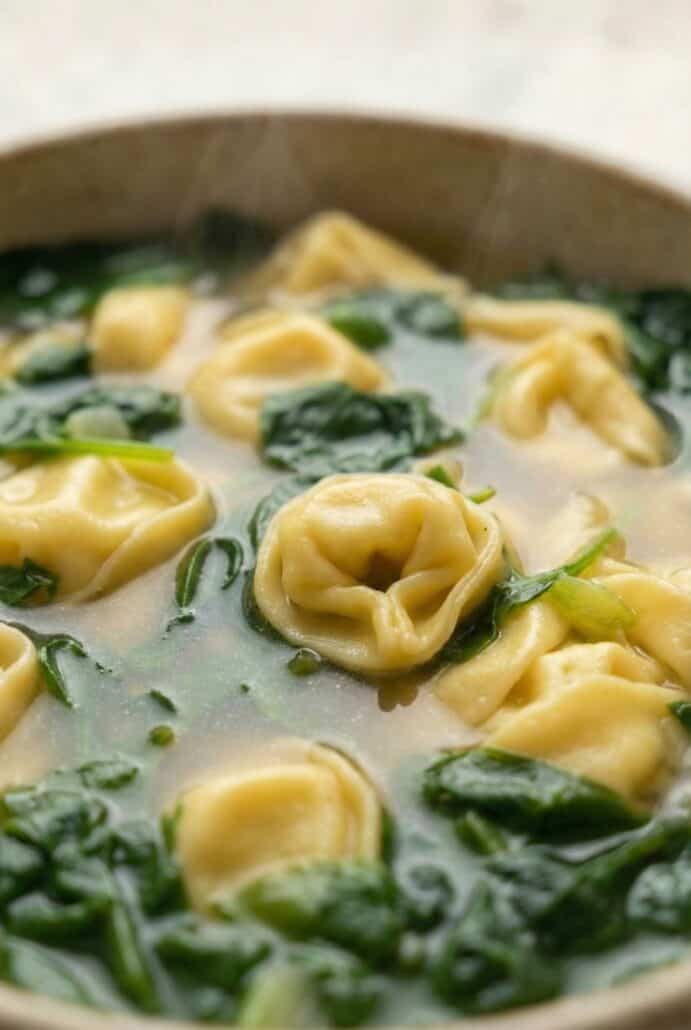 Close-up of tender cheese tortellini and fresh spinach in savory broth, showcasing this easy homemade spinach tortellini soup perfect for a quick weeknight dinner.