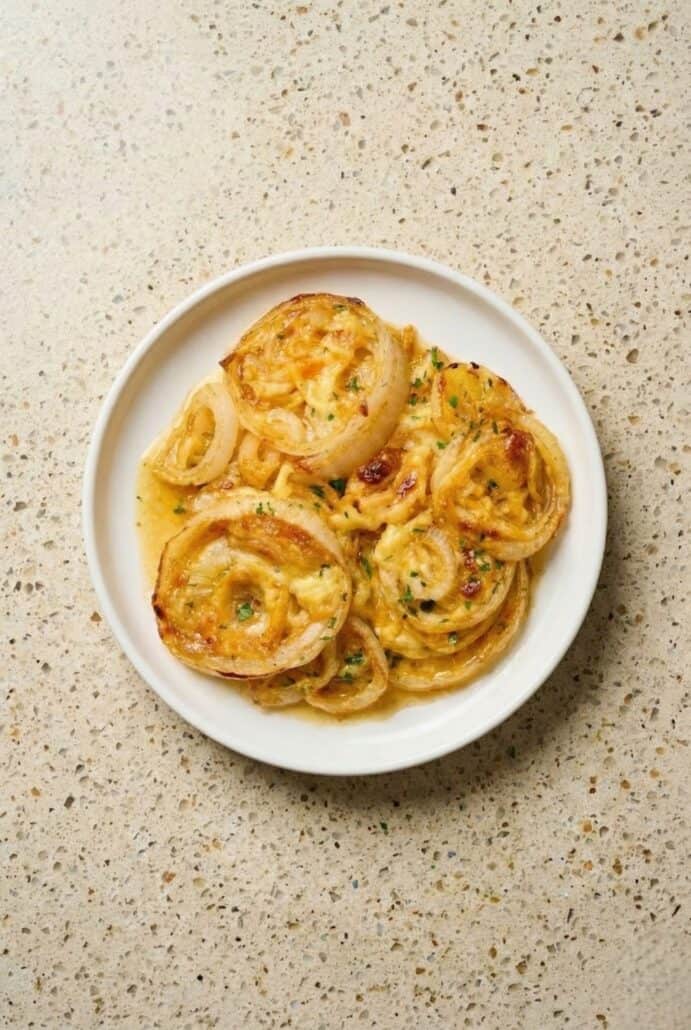 Plate of baked Tennessee Onions topped with melted cheddar and herbs, featuring tender sweet onion rings served as a cheesy Southern side dish.
